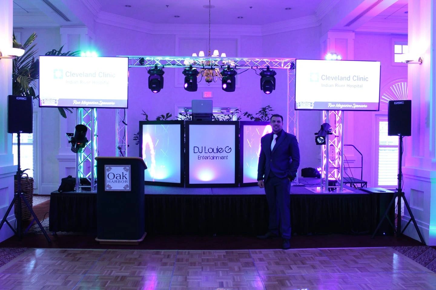 Man in suit stands near DJ Louie G Entertainment setup with Cleveland Clinic screens.